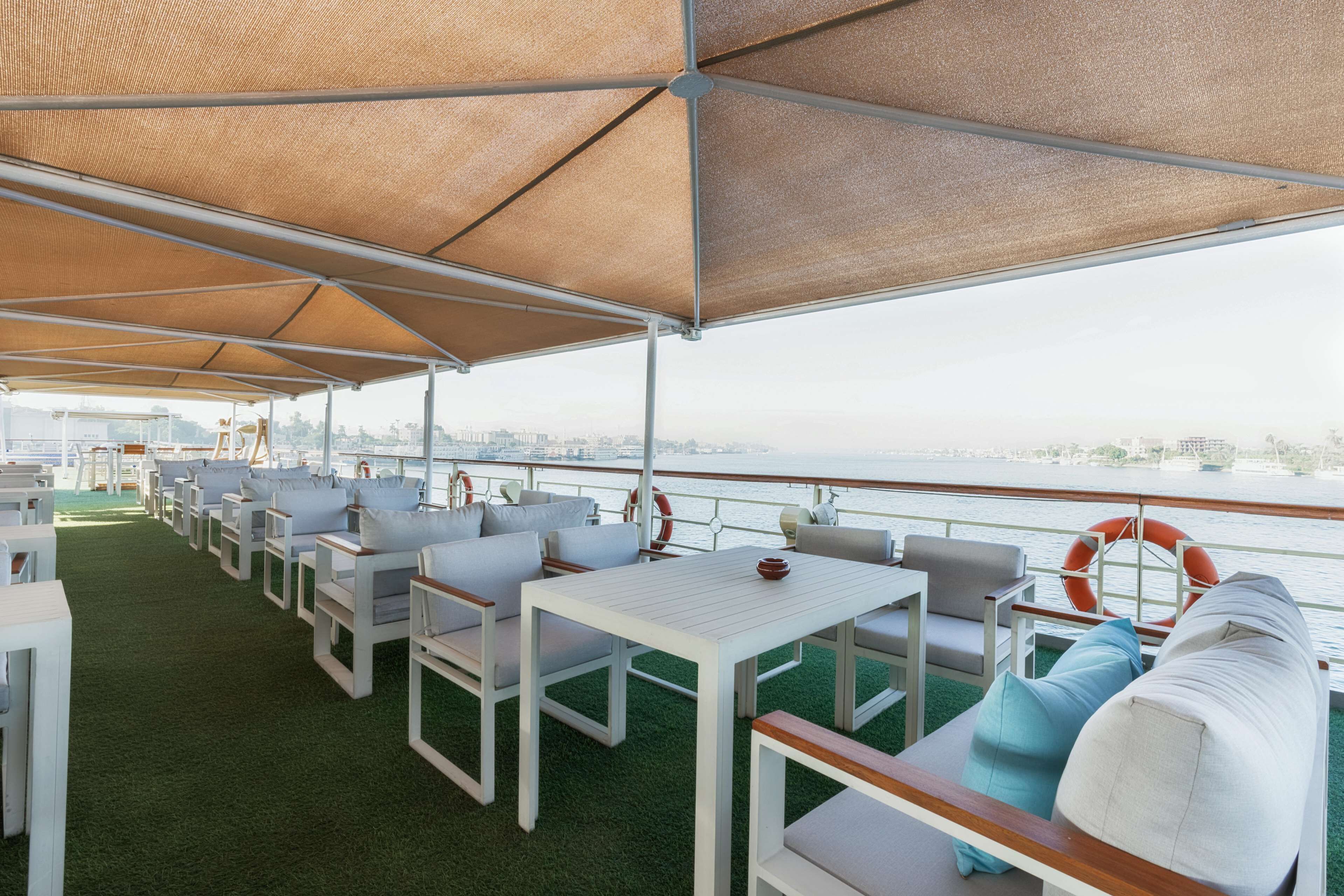 A covered outdoor seating area with white furniture and a view of the water.