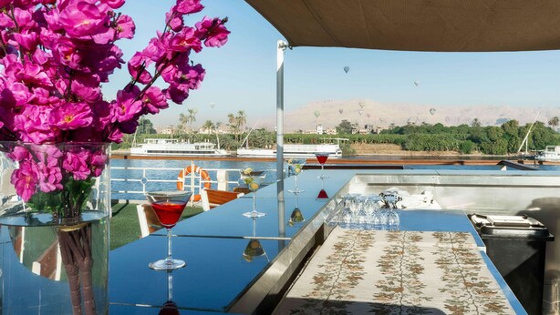 Un espace aménagé au bord de la piscine, avec une table, des chaises et un vase rempli de fleurs roses.