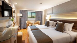 Une chambre d’hôtel avec deux lits, une télévision, un bureau avec un plateau en verre et une fenêtre avec des rideaux.