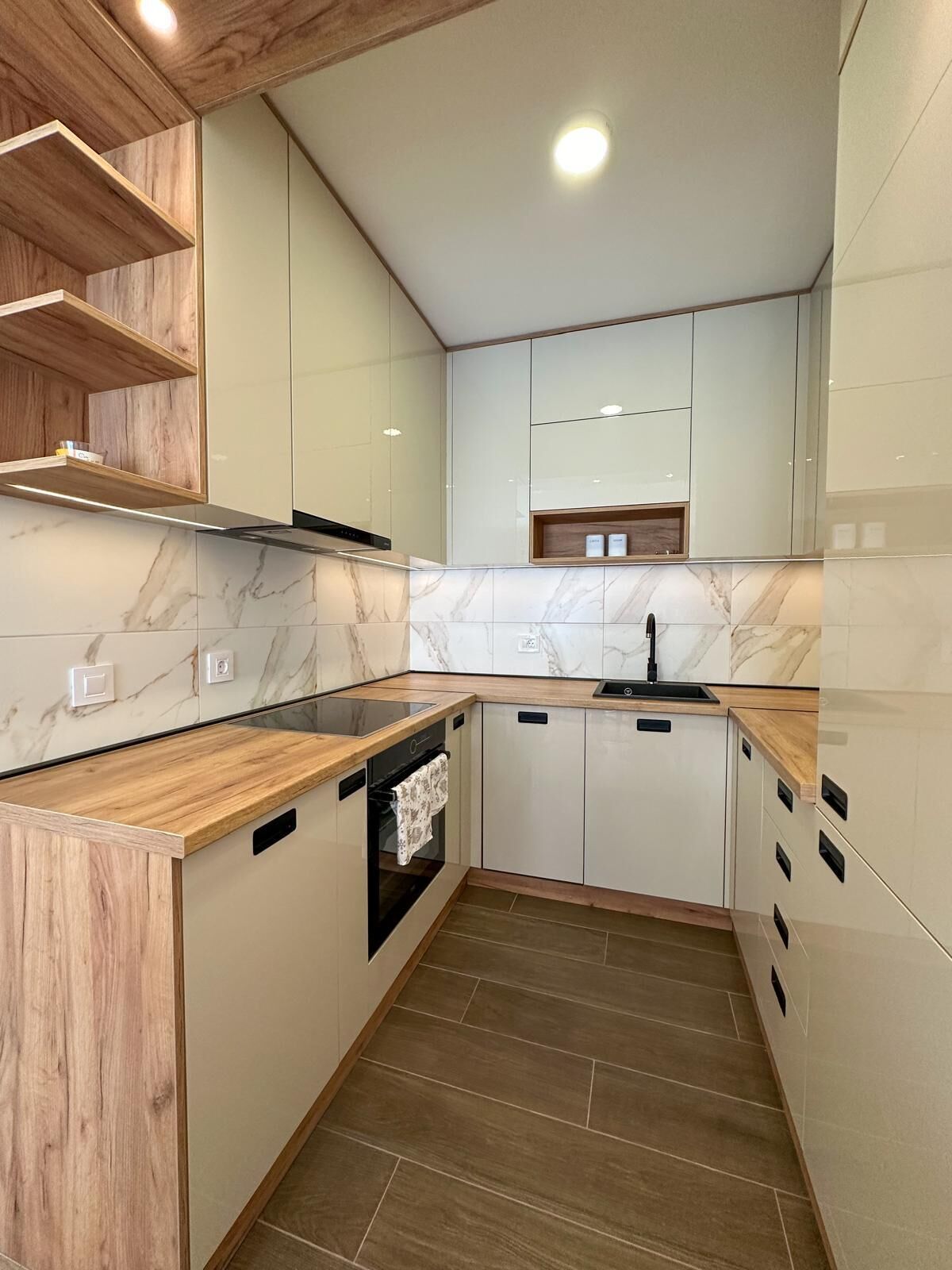 Una cocina moderna con encimeras de mármol, estanterías de madera y armarios empotrados.