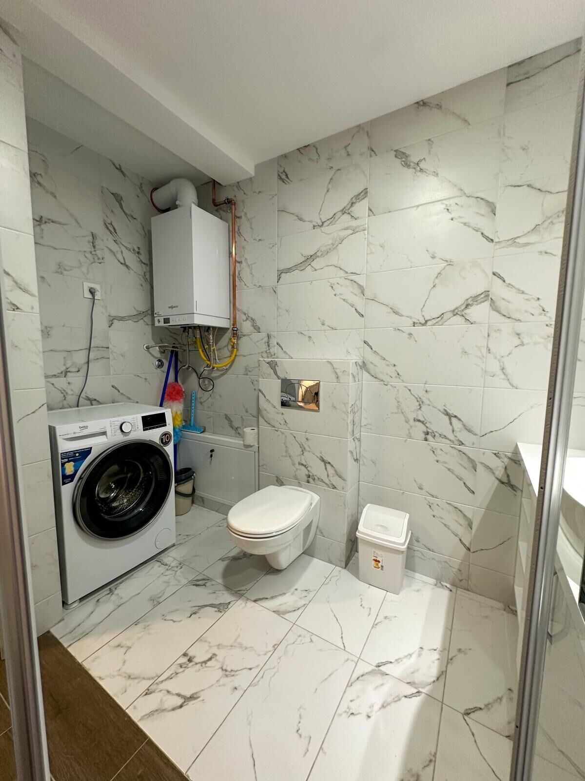 A compact bathroom with a washing machine, toilet, and a small storage unit.