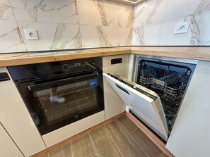Una cocina compacta con horno empotrado y lavavajillas, salpicadero de mármol y encimera de madera.