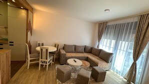 A modern living room with a sectional sofa, a round coffee table, and a dining area with chairs and a table. - I&I 3 Bedrooms Apartment (Kragujevac)