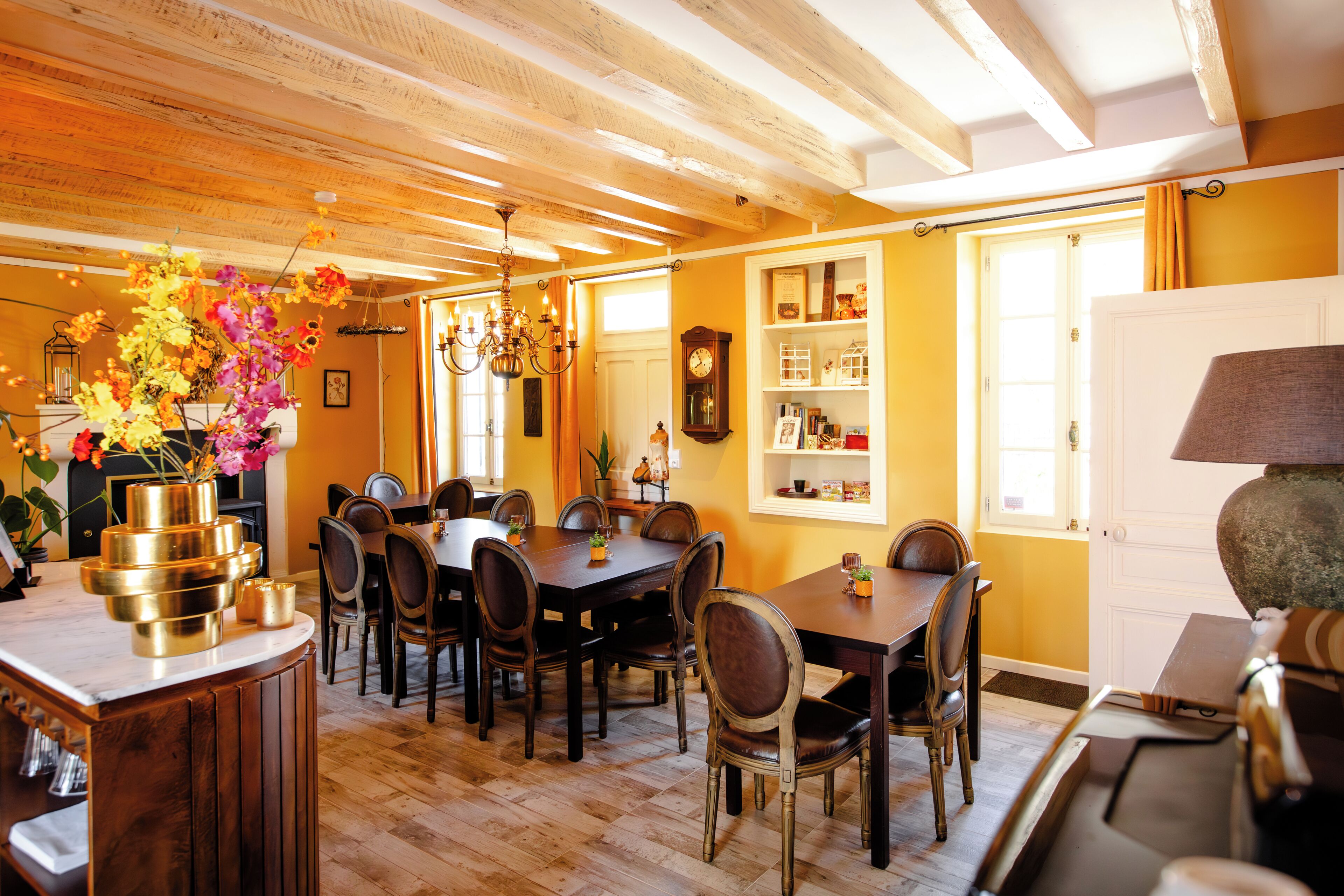 A dining area with wooden tables and chairs, a chandelier, and a clock on the wall.