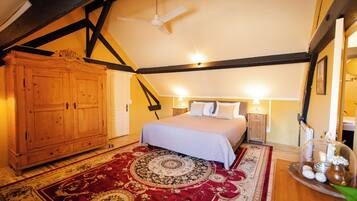A bedroom with a large bed, a wooden wardrobe, a ceiling fan, and a decorative rug.