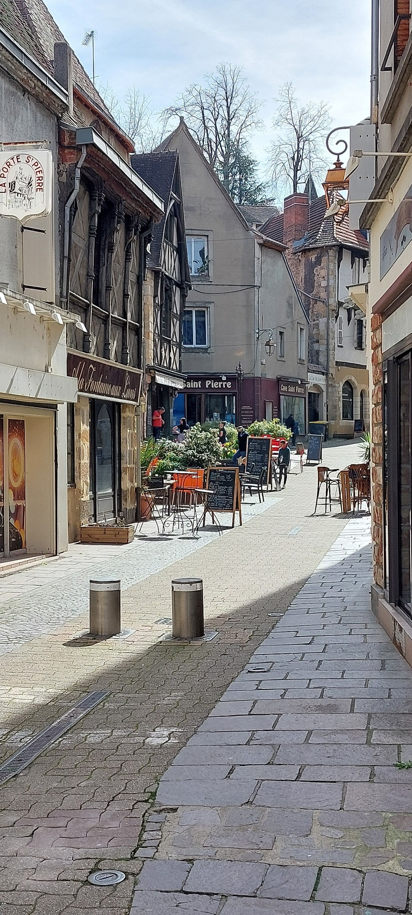 A cobblestone street with historic buildings, outdoor seating, and a café.