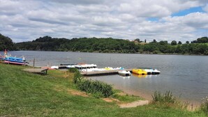 Un lago tranquillo con barche ormeggiate al molo, circondato da una vegetazione lussureggiante e colline.