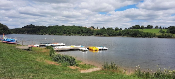 Un lago tranquilo con barcos amarrados en un muelle, rodeado de exuberante vegetación y colinas.