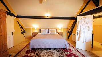 A bedroom with a bed, two bedside lamps, a ceiling fan, a wooden wardrobe, and a robe hanging on the door.