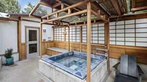 Un bain à remous avec des poutres en bois, un sol carrelé et un banc en bois.