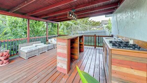 Um deck de madeira com churrasqueira, área de estar ao ar livre e vasos com plantas.