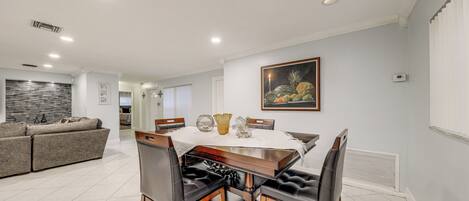 A dining area with a wooden table, black leather chairs, and a white tablecloth. There is a painting on the wall and a sofa in the background.