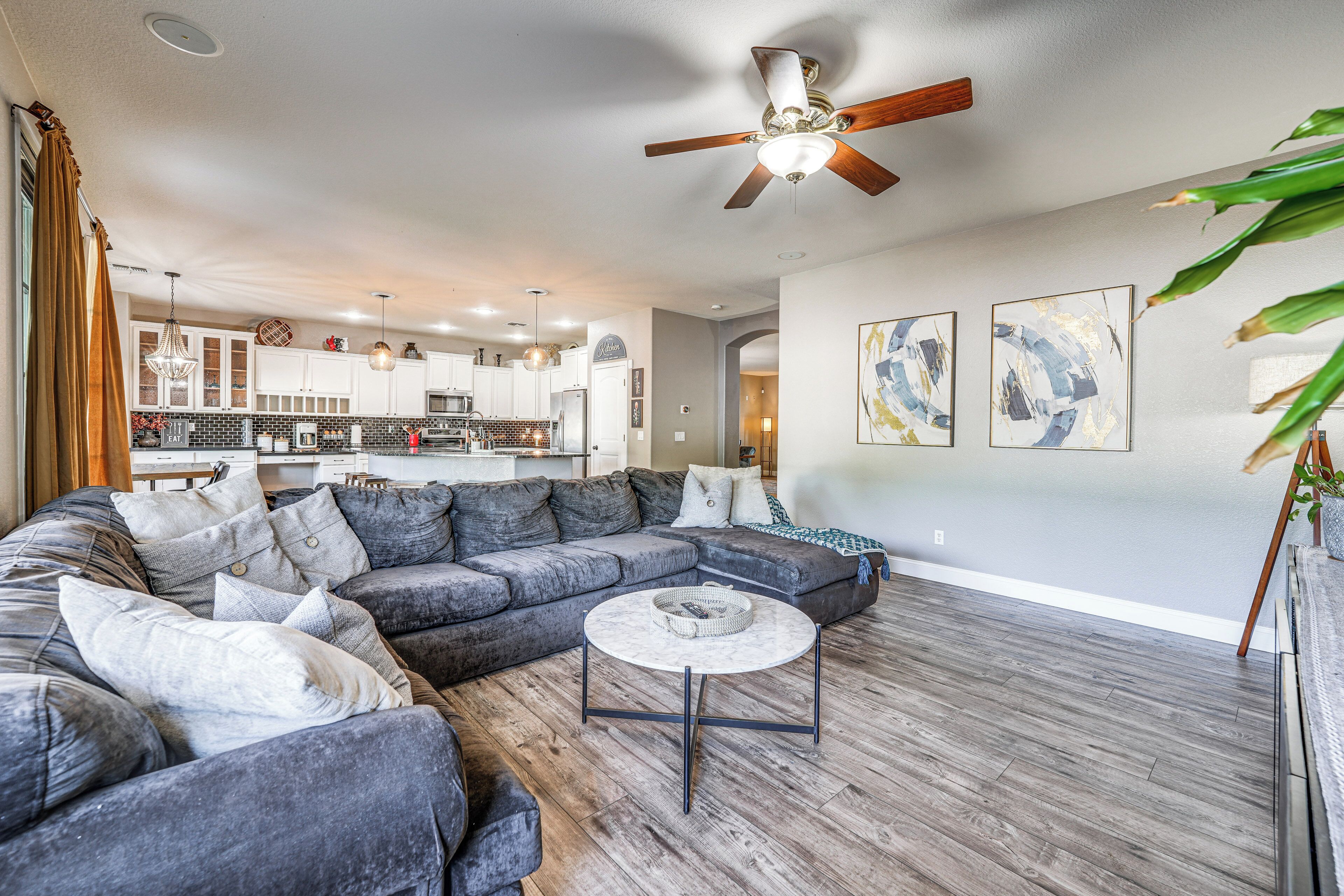 A spacious living room with a sectional sofa, a round coffee table, and a ceiling fan.