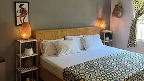 Camera luminosa con un letto, due abat-jour, una ventola a soffitto e una mensola a parete con oggetti decorativi.
