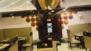 A restaurant interior with booths, tables, and a decorative ceiling. - Hotel JS (Dera Bassi)