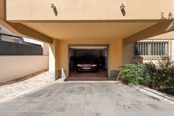 A car parked under a covered parking area with a tiled floor and a beige wall.
