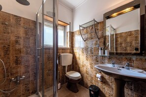 A bathroom with a glass shower enclosure, a toilet, a sink, and a large mirror.