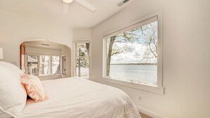 A bedroom with a large window offering a view of a lake and trees. - Colcord Point Sunset Cottage and Guest Cottage (Okoboji)