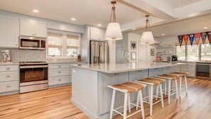 A modern kitchen with white cabinets, a central island with bar stools, stainless steel appliances, and pendant lighting. - Colcord Point Sunset Cottage and Guest Cottage (Okoboji)