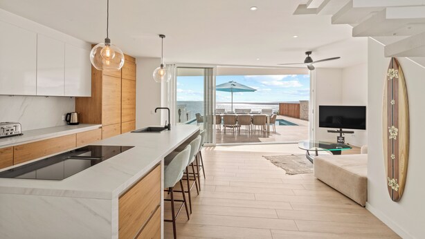 A modern kitchen with a central island, wooden cabinets, and a large window overlooking a pool.