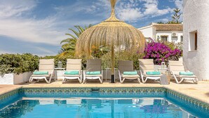 Une piscine avec des chaises longues et un parasol en chaume.