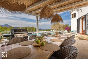 An outdoor dining area with a grill, wicker furniture, and a view of the mountains. - Villa MOBA by Abahana  Villas (Javea / Xàbia)