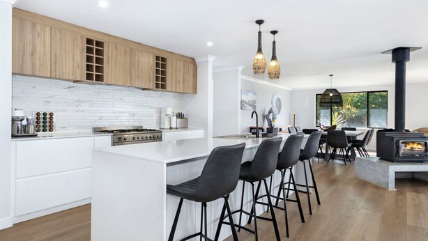 A modern kitchen with a central island, bar stools, a stove, and a wood-burning stove.