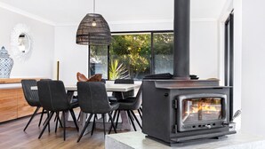 A modern kitchen with a wood-burning stove, black chairs, a dining table, and a hanging light fixture.