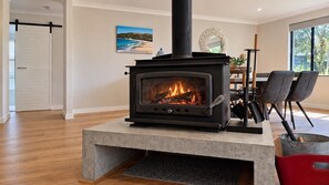 A modern living room with a wood-burning stove, a dining area with chairs, a table, and a view of the outdoors.