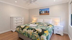 A bedroom with a bed, a nightstand, a dresser, a ceiling fan, and a painting on the wall. - Charming Pet-Friendly Retreat Near Quindalup's Pristine Beaches – Perfect for Families & Friends! (Quindalup)