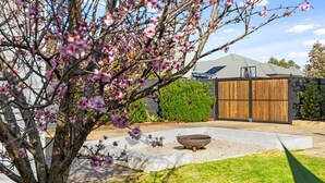 A residential property with a large wooden gate, a concrete patio, and a tree with pink blossoms.