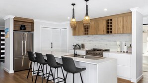 A modern kitchen with a central island, bar stools, stainless steel appliances, and wooden cabinets.