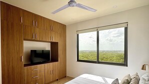 A bedroom with a bed, wooden wardrobe, television, and a window with a view. - Apartment for Rent in Valle Aurora 2 BDR 8 min from the Sea! (Playa del Carmen)