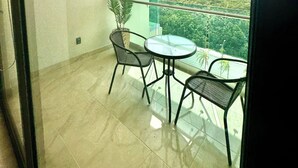 A balcony with a glass table and chairs, a potted plant, and a view of a green landscape. - Apartment for Rent in Valle Aurora 2 BDR 8 min from the Sea! (Playa del Carmen)