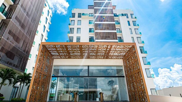 A modern building with a large entrance, glass doors, and a wooden decorative structure in front. - Apartment for Rent in Valle Aurora 2 BDR 8 min from the Sea! (Playa del Carmen)