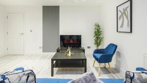 A modern living room with a television displaying 'NETFLIX', a blue armchair, a small table with a decorative item, and a potted plant. - Modern 1BR Flat | Walkable High Street Stay (Southend-on-Sea)
