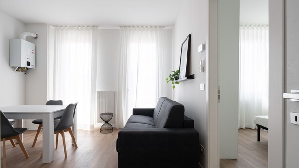 A modern living room with a black sofa, a dining table with chairs, and a white radiator. - Carducci Modern Apartment 7 by Wonderful Italy (Mestre)