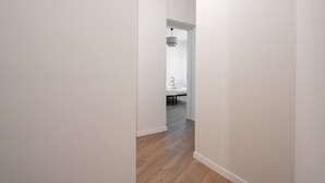Un pasillo estrecho con suelo de madera que conduce a un dormitorio con cama y una lámpara colgante.