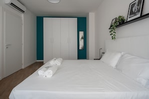 Ein Hotelzimmer mit einem großen Bett, weißen Leinentüchern, türkisfarbenen Akzentwänden, einem Kleiderschrank und einer Zimmerpflanze.