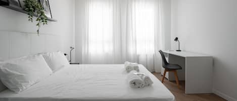 A minimalist hotel room with a neatly made bed, a desk, and a chair.