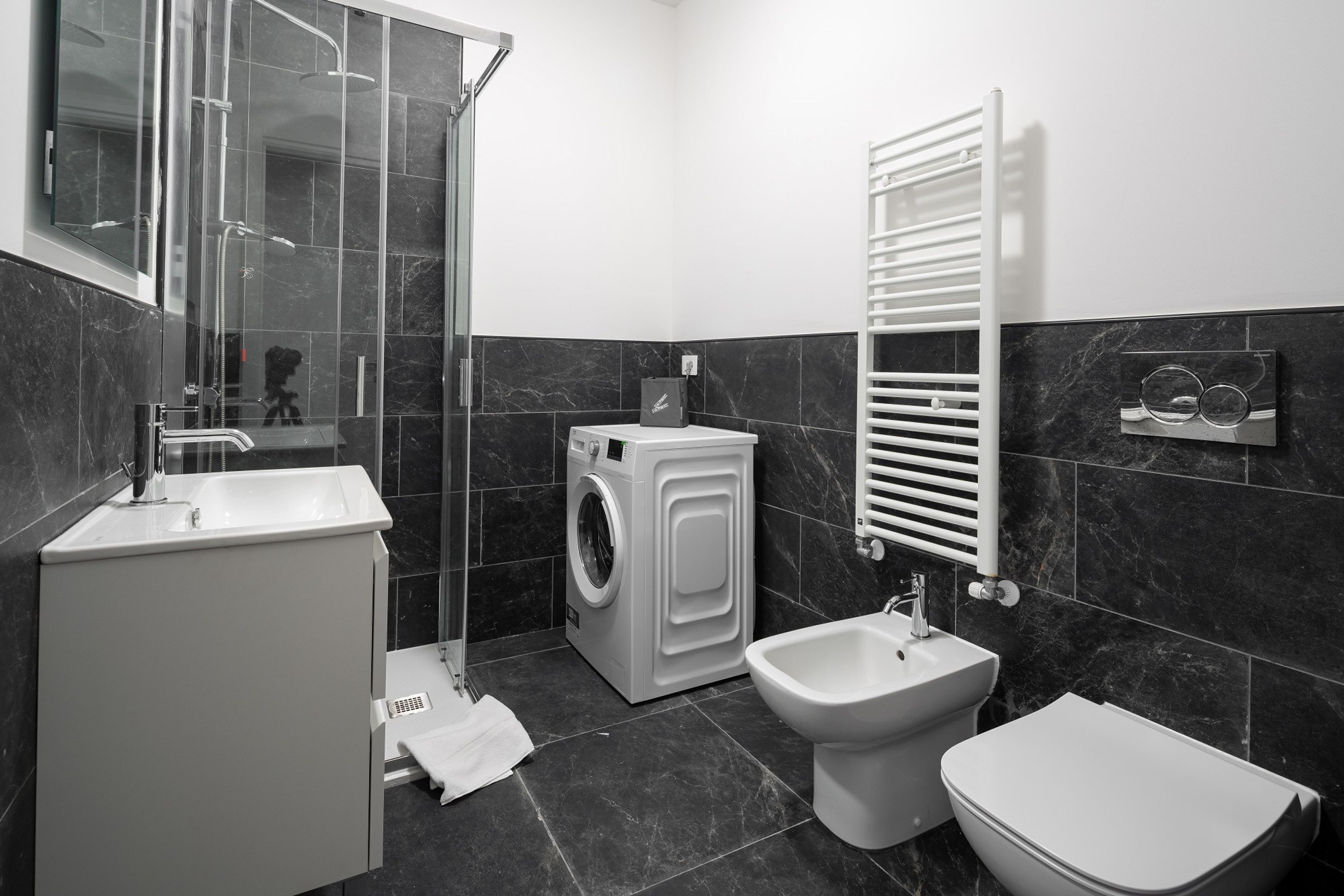 A modern bathroom with a glass shower enclosure, a washing machine, a bidet, and a toilet.