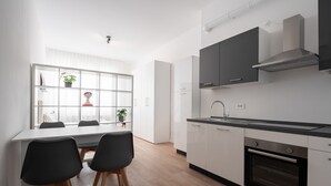 Una cocina moderna con gabinetes blancos, una encimera negra y un horno empotrado. Cuenta con un comedor con mesa y sillas.