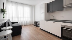 A modern kitchen with white cabinets, a black countertop, and a built-in oven. There is a dining area with a black sofa and two white stools. - Carducci Modern Apartment 1 by Wonderful Italy (Mestre)
