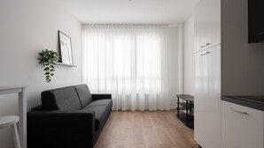 A modern, minimalistic living space with a black sofa, a small white table, and a kitchen area with white cabinets and a black countertop. - Carducci Modern Apartment 1 by Wonderful Italy (Mestre)
