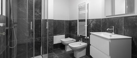 A modern bathroom with a glass-enclosed shower, a white sink, a bidet, and a towel rack.