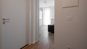 Egy folyosó, fa parkettel, fehér falakkal és egy bal oldali ajtóval.