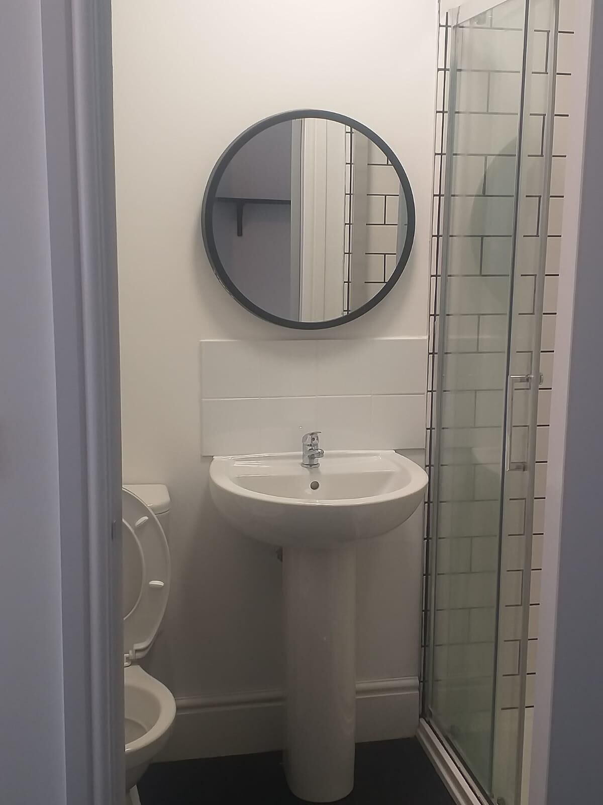 A bathroom with a white sink, a round mirror, and a glass shower enclosure.