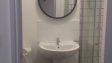 A bathroom with a white sink, a round mirror, and a glass shower enclosure.