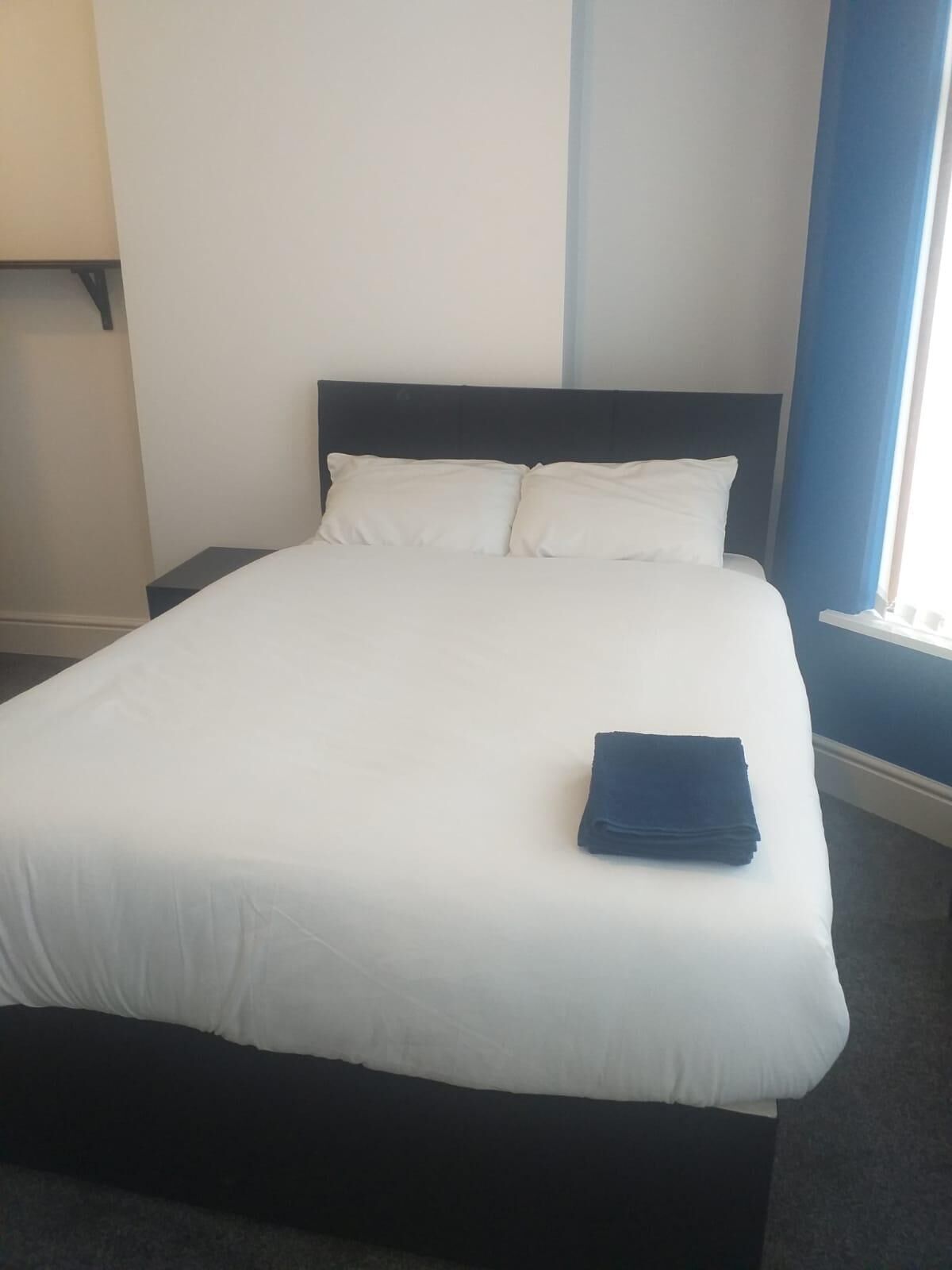 A neatly made bed with white linens and a folded dark blue towel on the footboard.