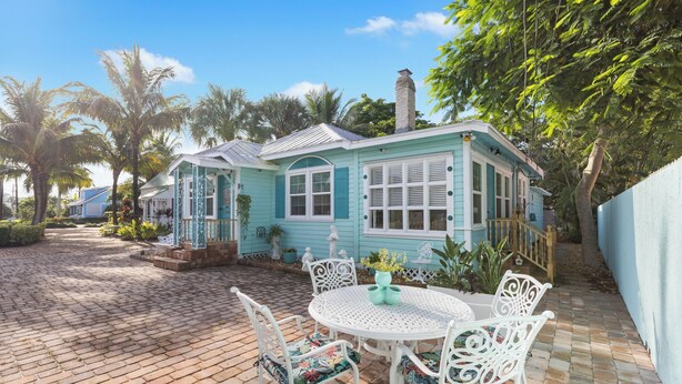 Een turquoise huis met een patio, voorzien van een ronde tafel en witte stoelen.